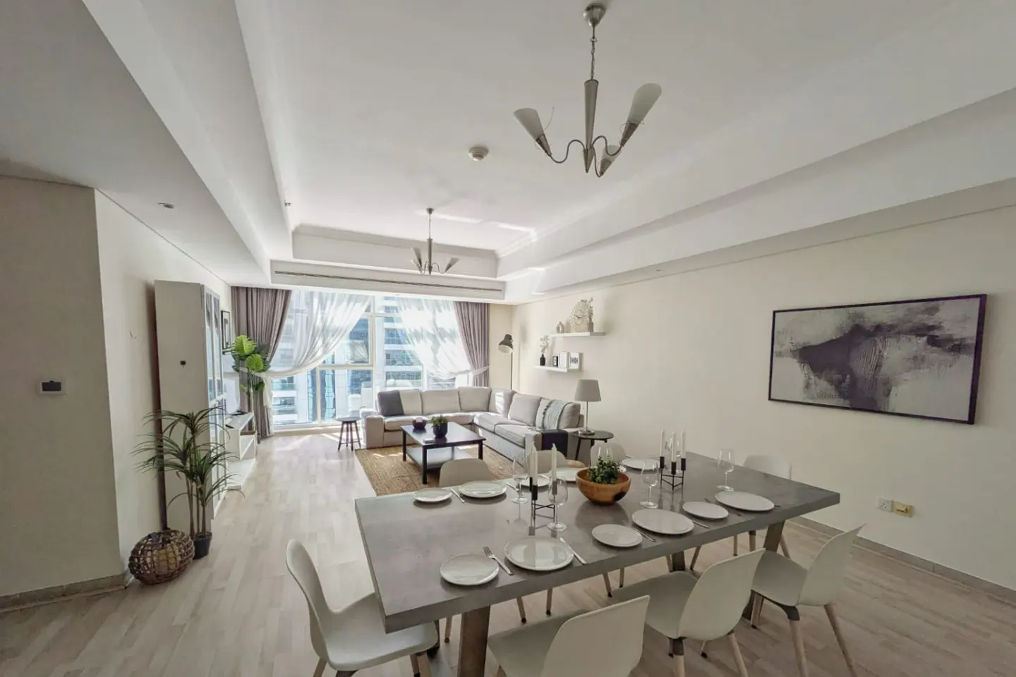 Modern open-plan living and dining area with a grey dining table, white chairs, and a sectional sofa by a bright window.