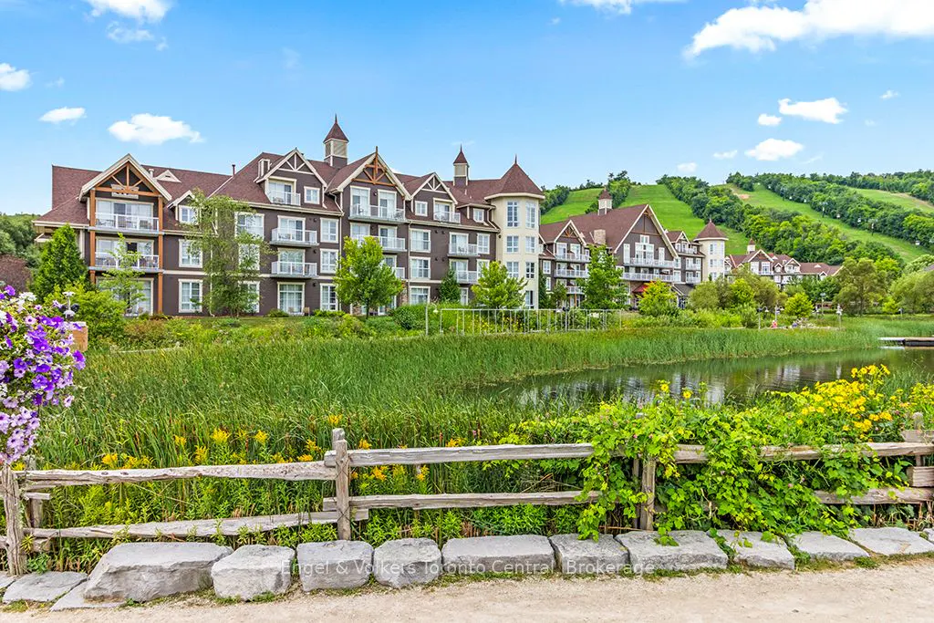 Exterior view of a brown and white condo building with balconies, overlooking a pond and green hillside.
