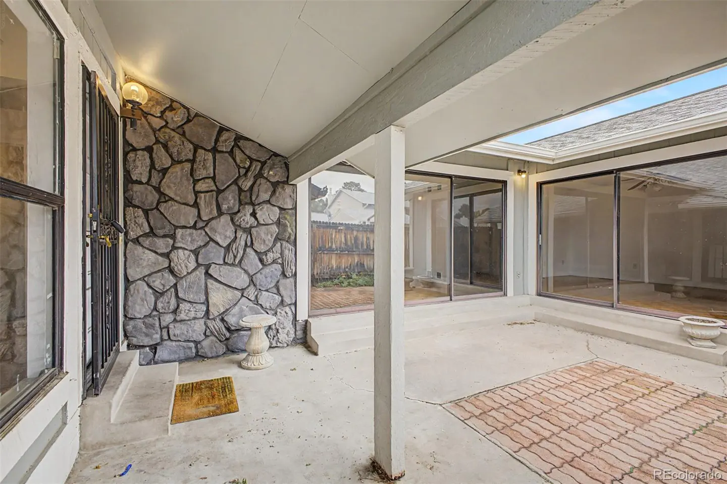 Covered patio with stone wall, concrete floor, and sliding glass doors leading to the interior. A small table sits near the wall.