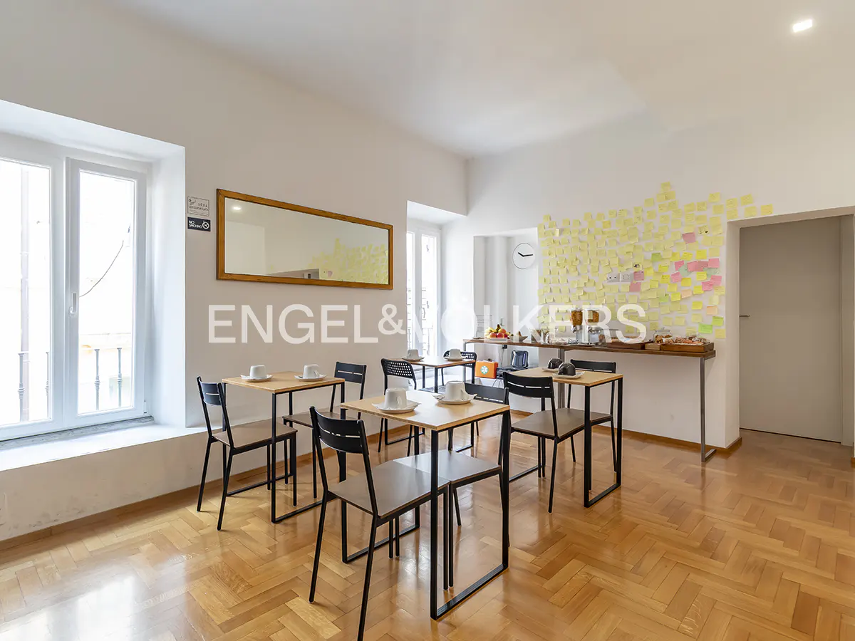 Bright room with wood floors, tables, and chairs. A buffet table with sticky notes is against the wall. A mirror hangs above the tables.