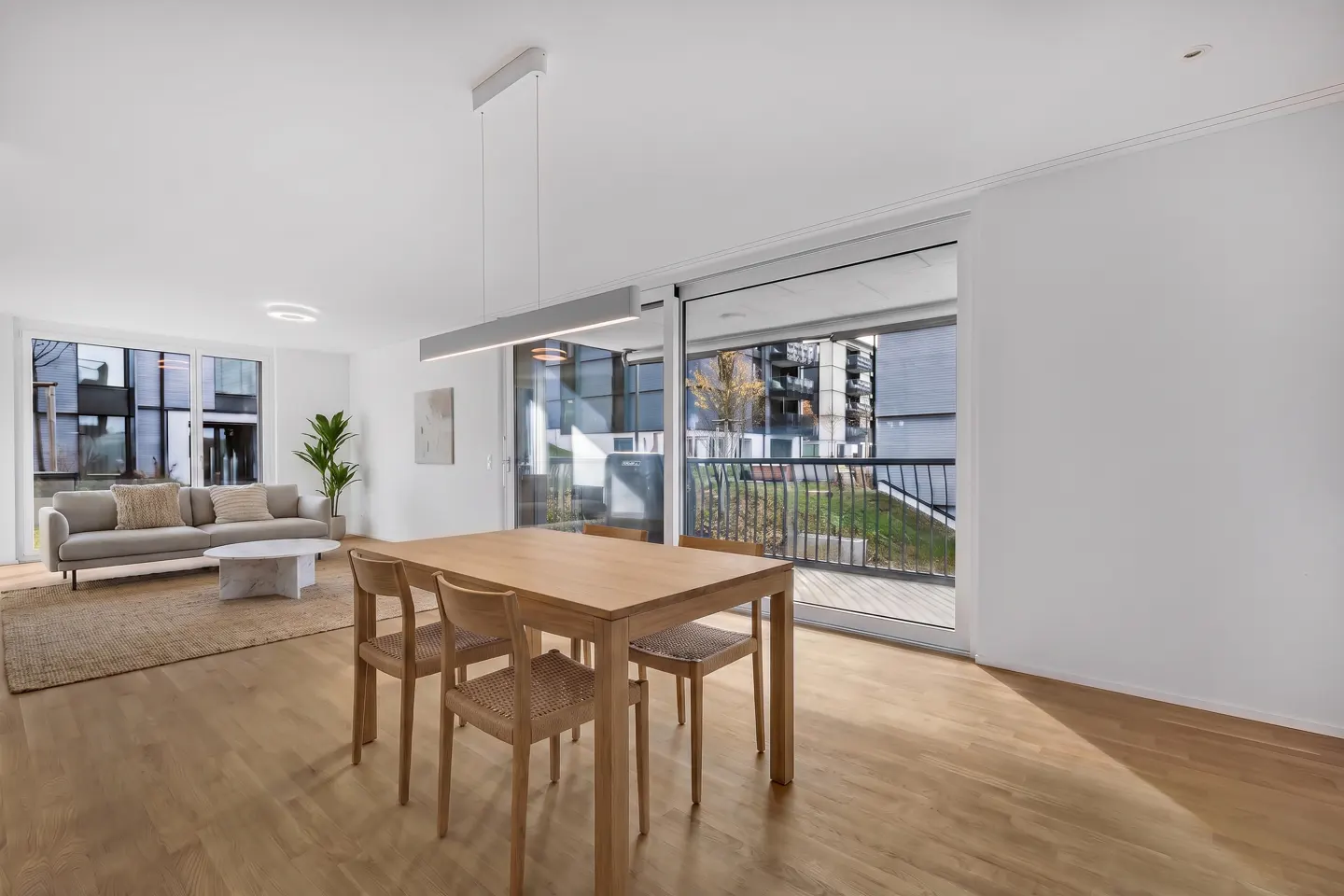 Bright, modern living and dining area with wood floors, table, and sofa. Sliding glass doors open to a balcony.