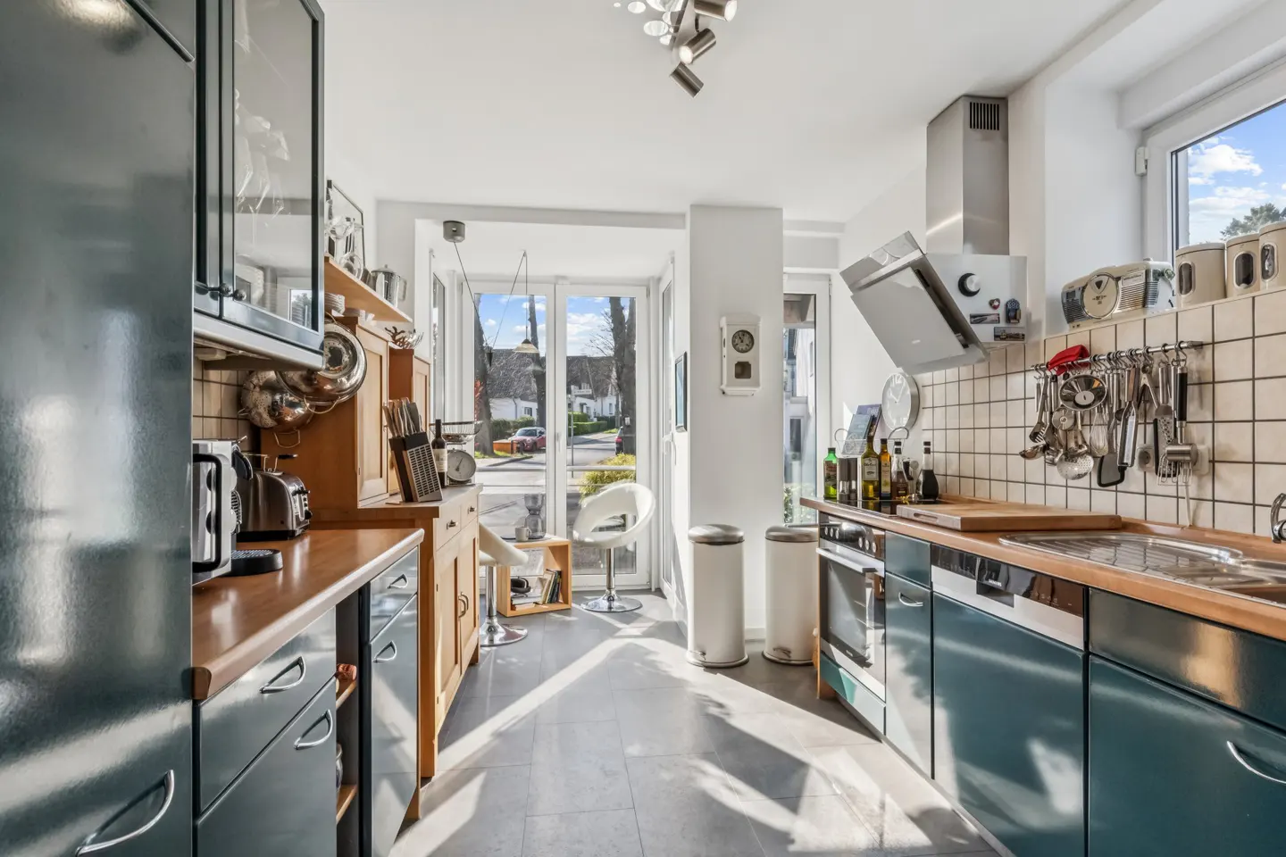 Bright kitchen with blue cabinets, wood countertops, and stainless steel appliances. A white chair sits near the glass doors.