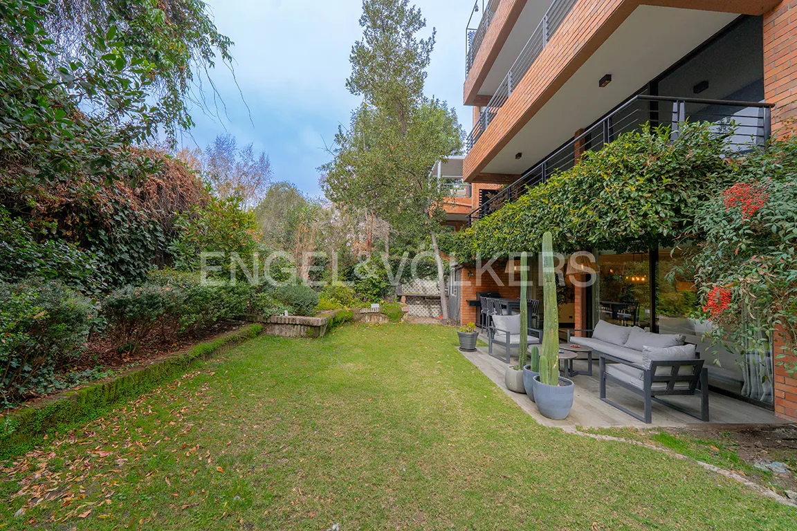 A grassy backyard with a patio featuring modern grey outdoor furniture, potted cacti, and a brick building with balconies.
