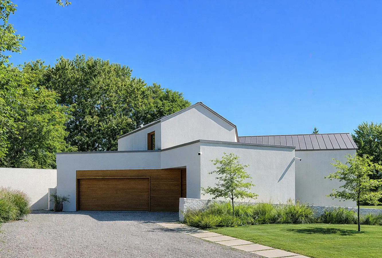 Modern white house with a brown wood garage door, gravel driveway, and green lawn under a clear blue sky.