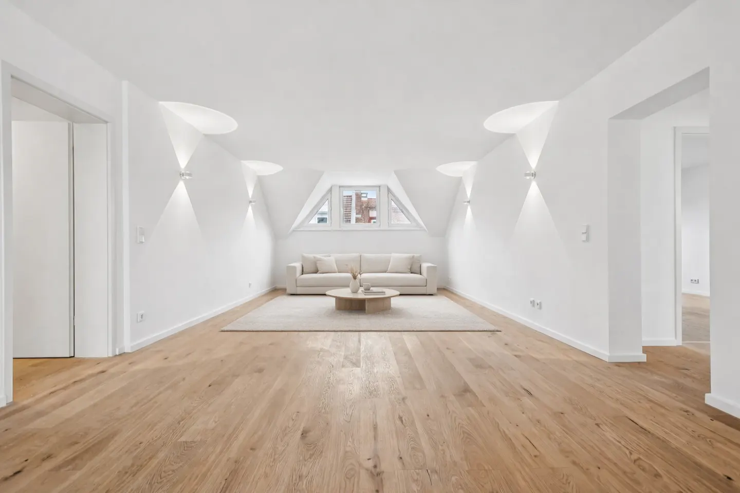 Bright, all-white living room with wood floors, a beige sofa, and a round coffee table on a light rug. A window is centered above the sofa.