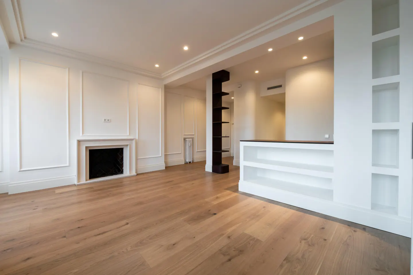 Bright, empty living room with hardwood floors, white walls, fireplace, and built-in shelving.