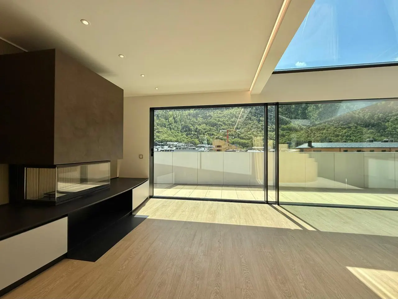 Bright, modern living room with a fireplace, wood floors, and sliding glass doors to a balcony with a mountain view.