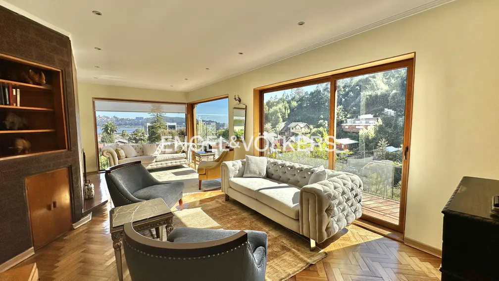 Living room with herringbone wood floors, grey sofas, and large windows with a view of trees and water.