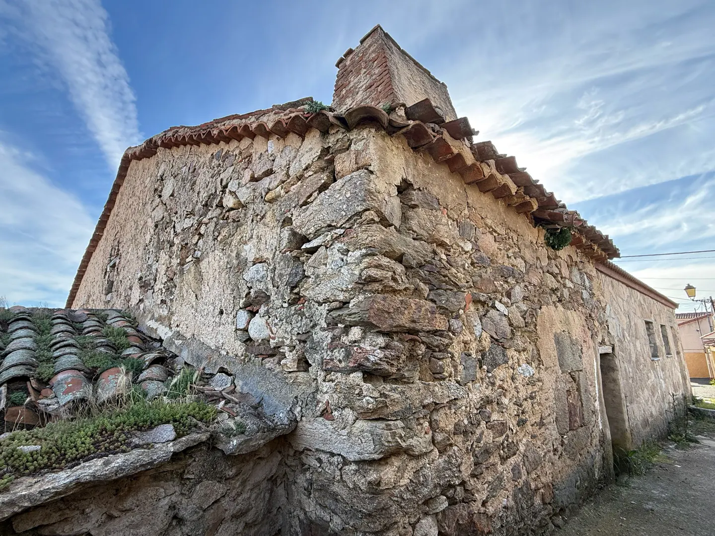Exterior view of an old stone house with a red tile roof under a blue sky with wispy clouds.
