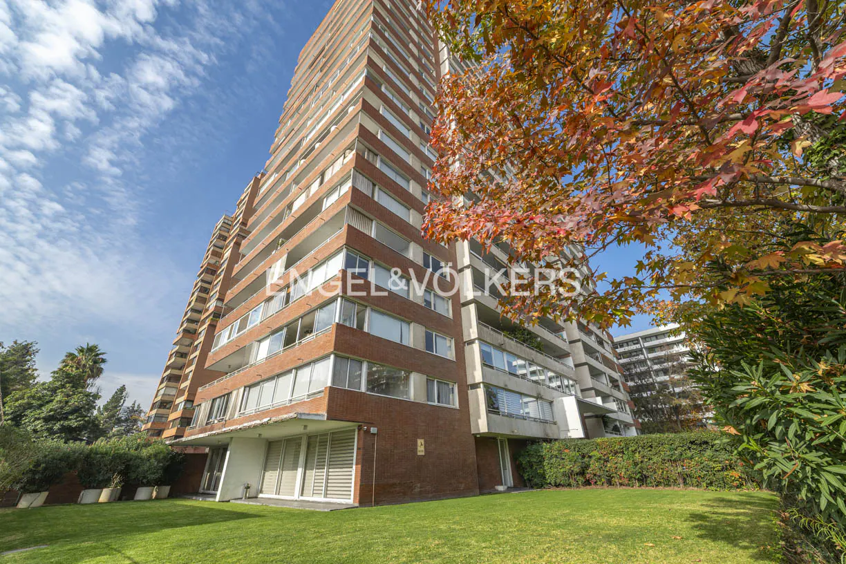 Exterior view of a tall brick apartment building with balconies, green lawn, and autumn foliage.