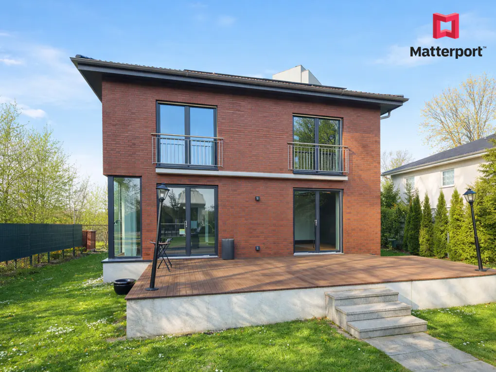 Two-story brick house with a wooden deck, gray trim, and small balconies under a blue sky.