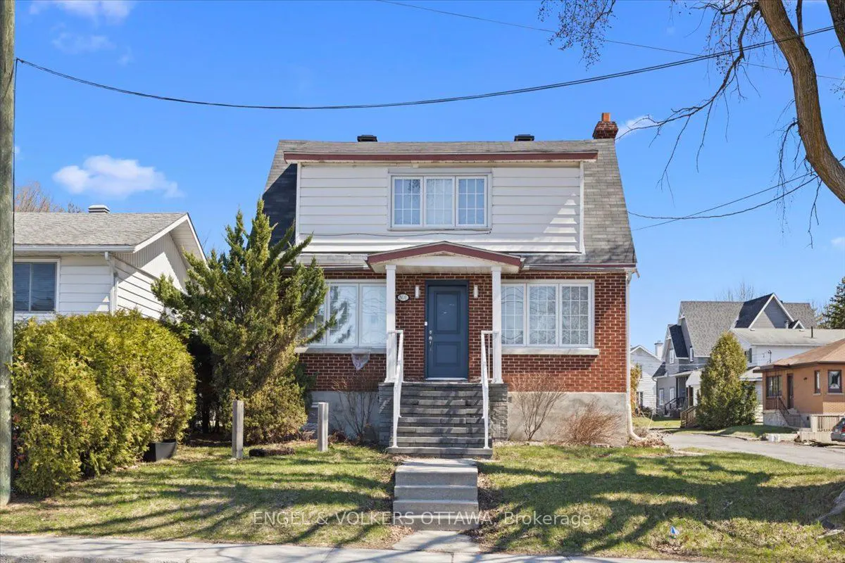 Two-story brick house with a blue door and white trim on a sunny day. Steps lead to the front porch. Green lawn and trees.