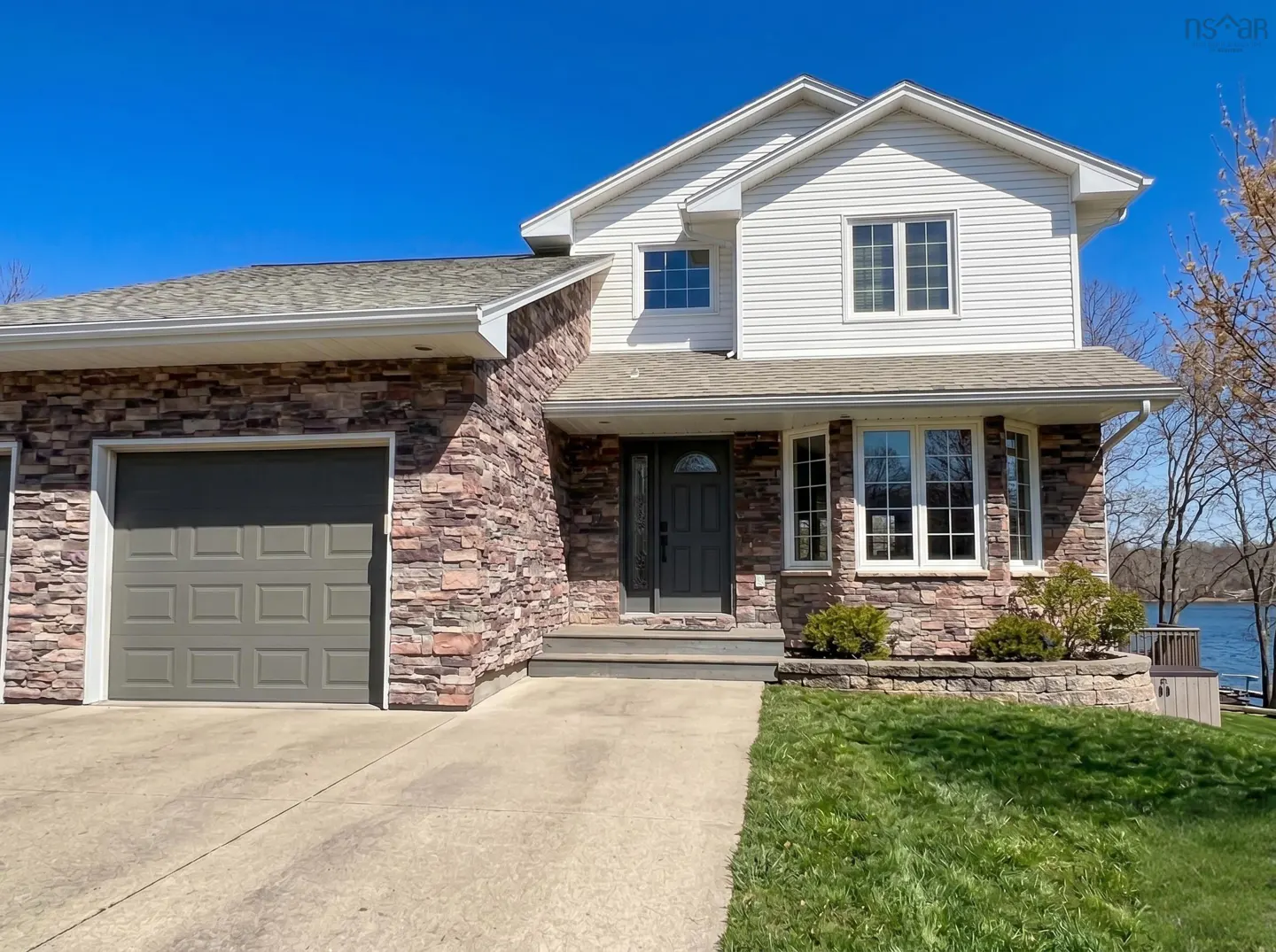 Two-story house with stone and white siding, a gray garage door, and a well-manicured lawn on a sunny day.