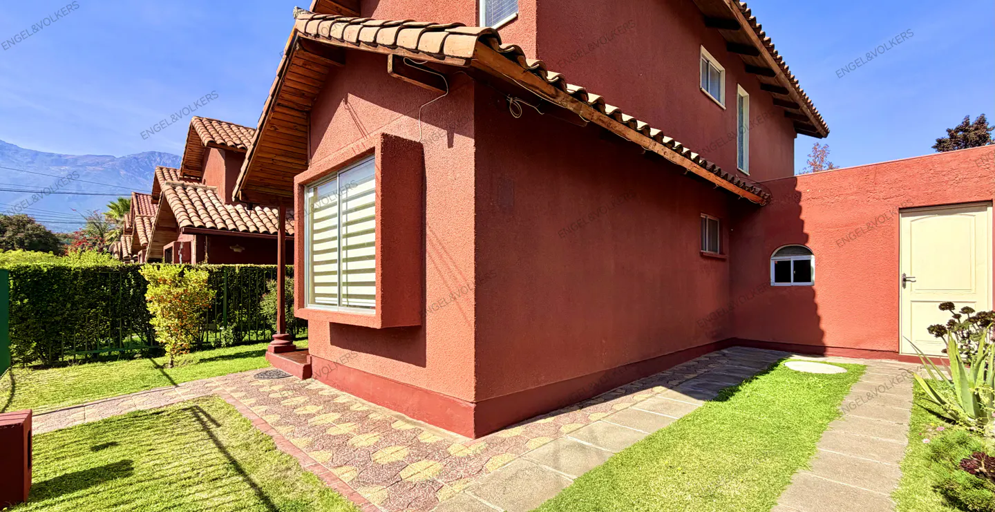 Exterior view of a red stucco house with a brown tile roof, green lawn, and a mountain in the background.