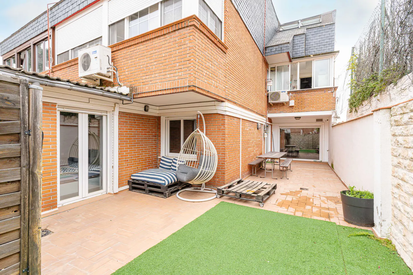 A backyard patio with a brick building, a hanging chair, and a pallet couch.