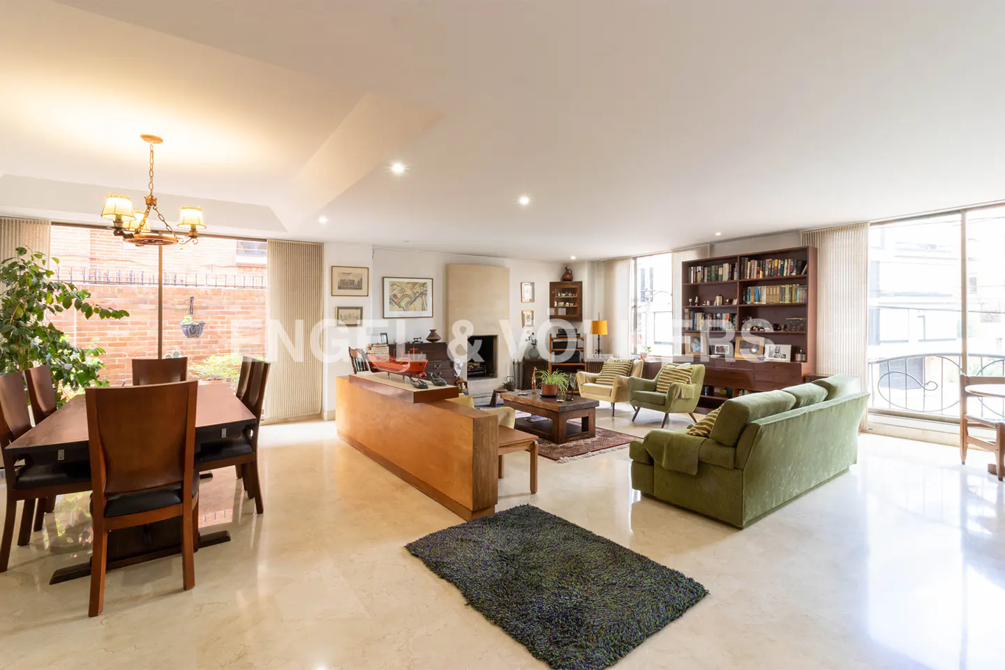 Open-concept living and dining area with a long wood table, green sofa, and fireplace.