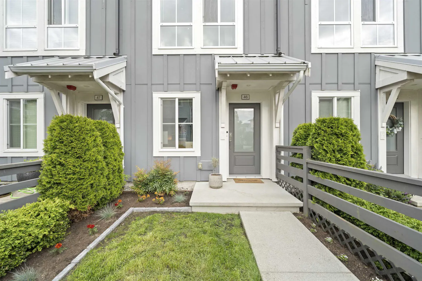 Gray townhouse exterior with white trim, a gray door, and a small front yard with green bushes and grass.