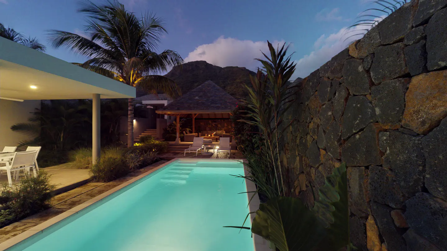 Outdoor pool at dusk with a gazebo, lounge chairs, and a stone wall. Palm trees and a mountain are in the background.