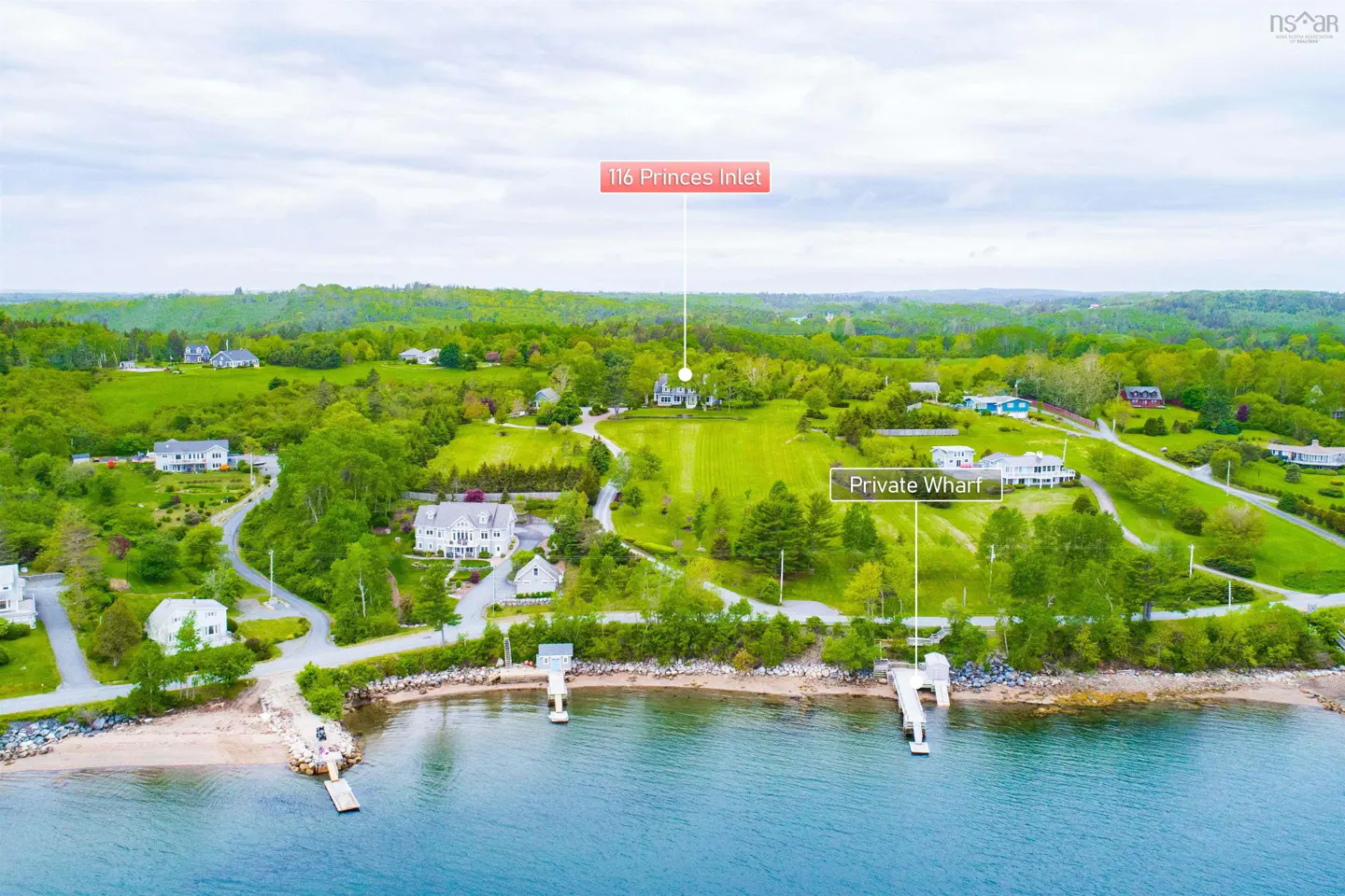Aerial view of waterfront property with green lawns, houses, and private wharfs on a blue bay.
