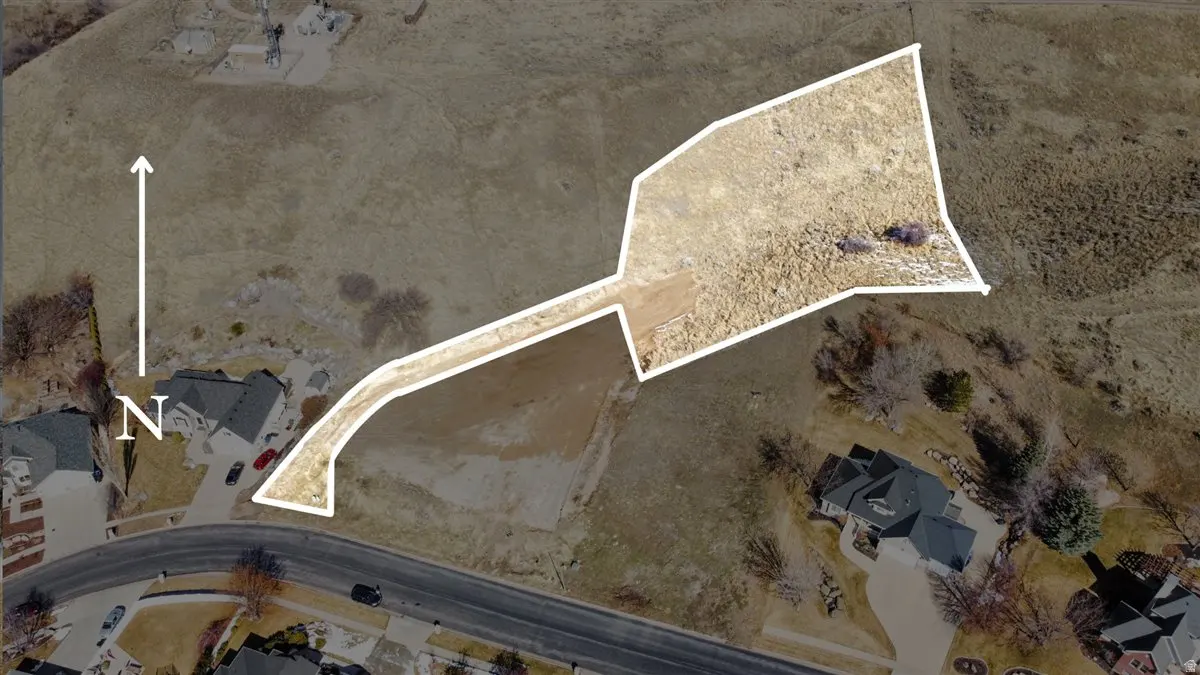 Aerial view of a vacant lot outlined in white, adjacent to houses and a road. A north arrow is visible.