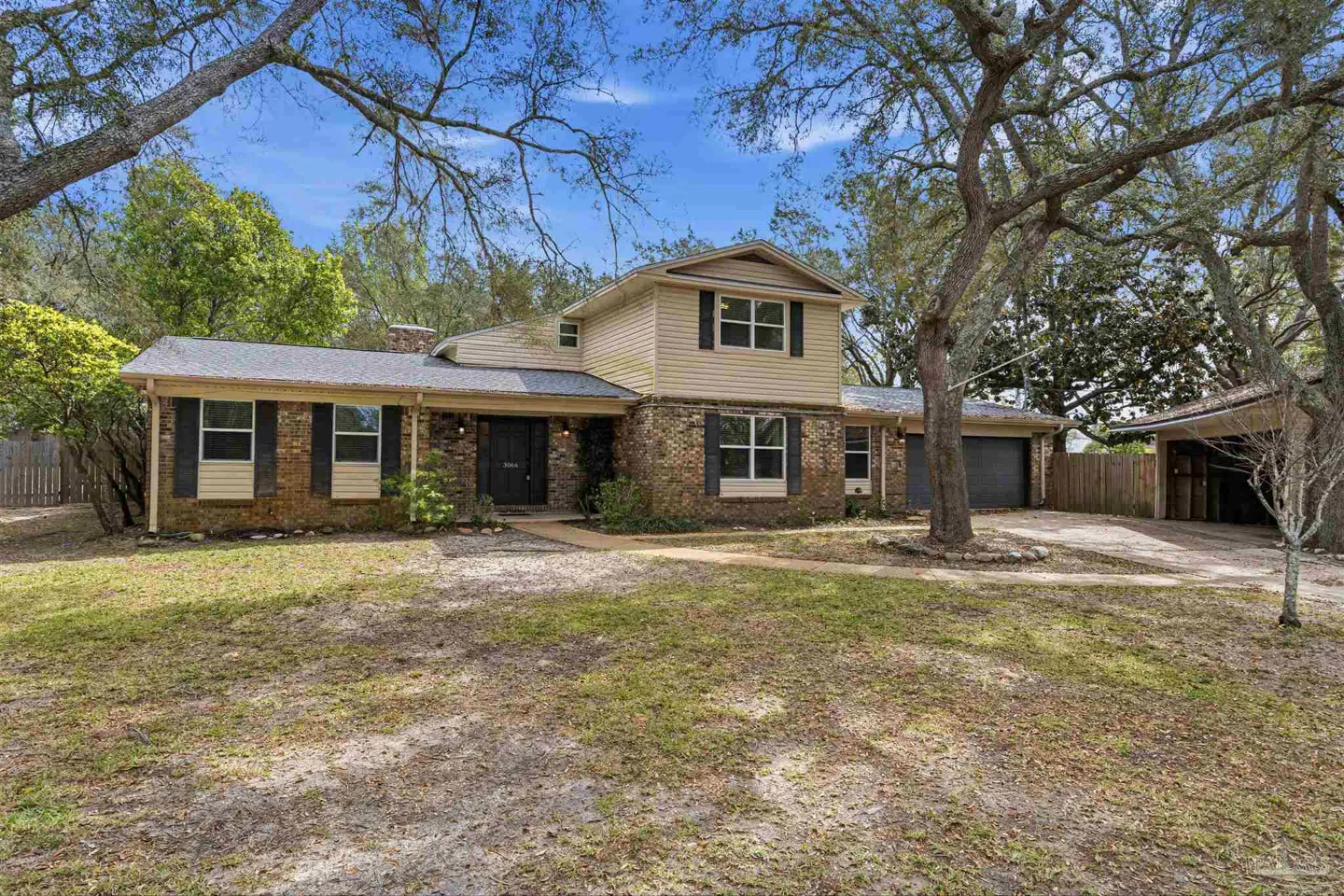 Two-story house with brick and beige siding, black shutters, and a gray roof, surrounded by trees.