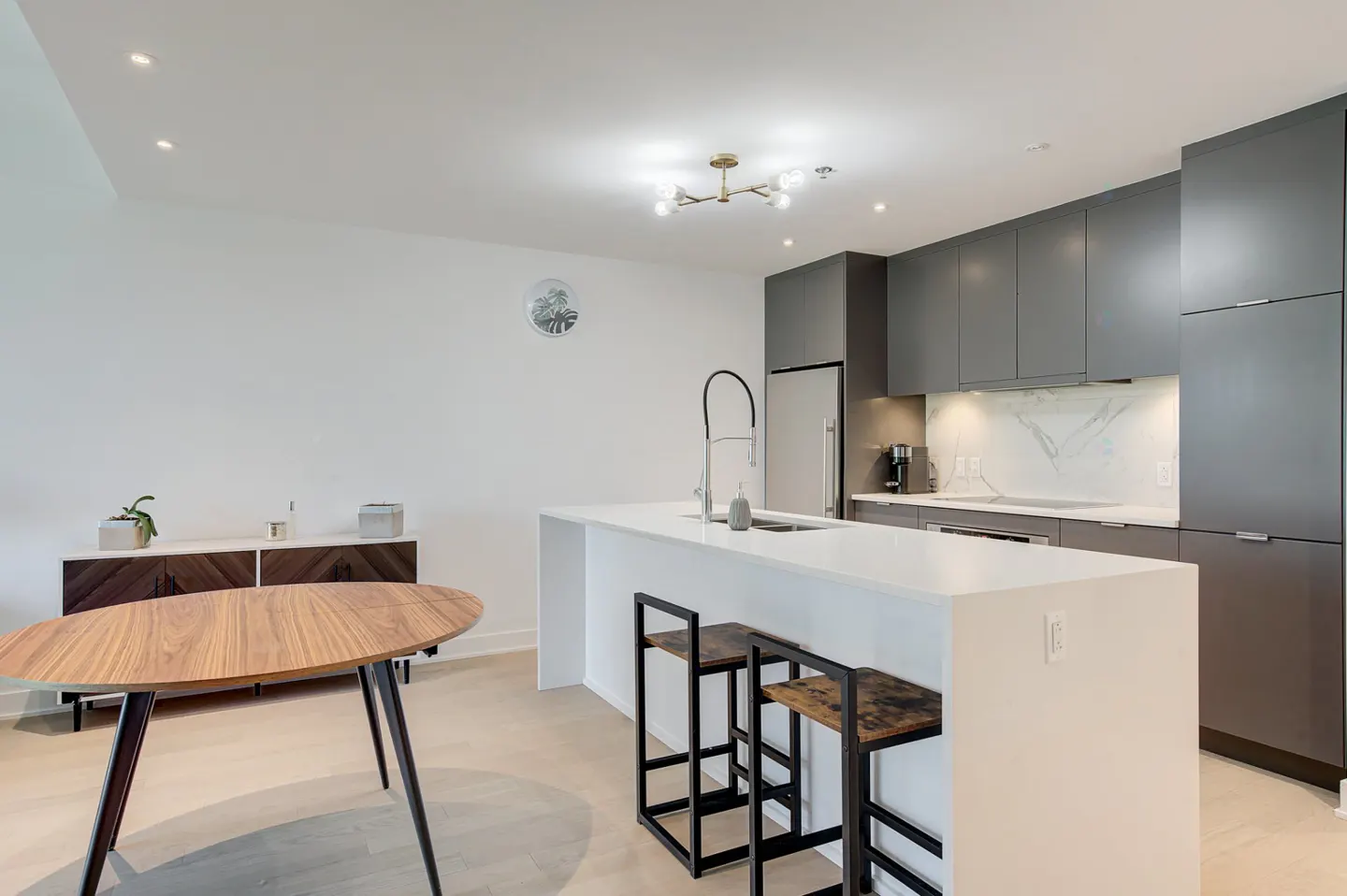 A modern kitchen with gray cabinets, a white island with stools, and a wooden table.