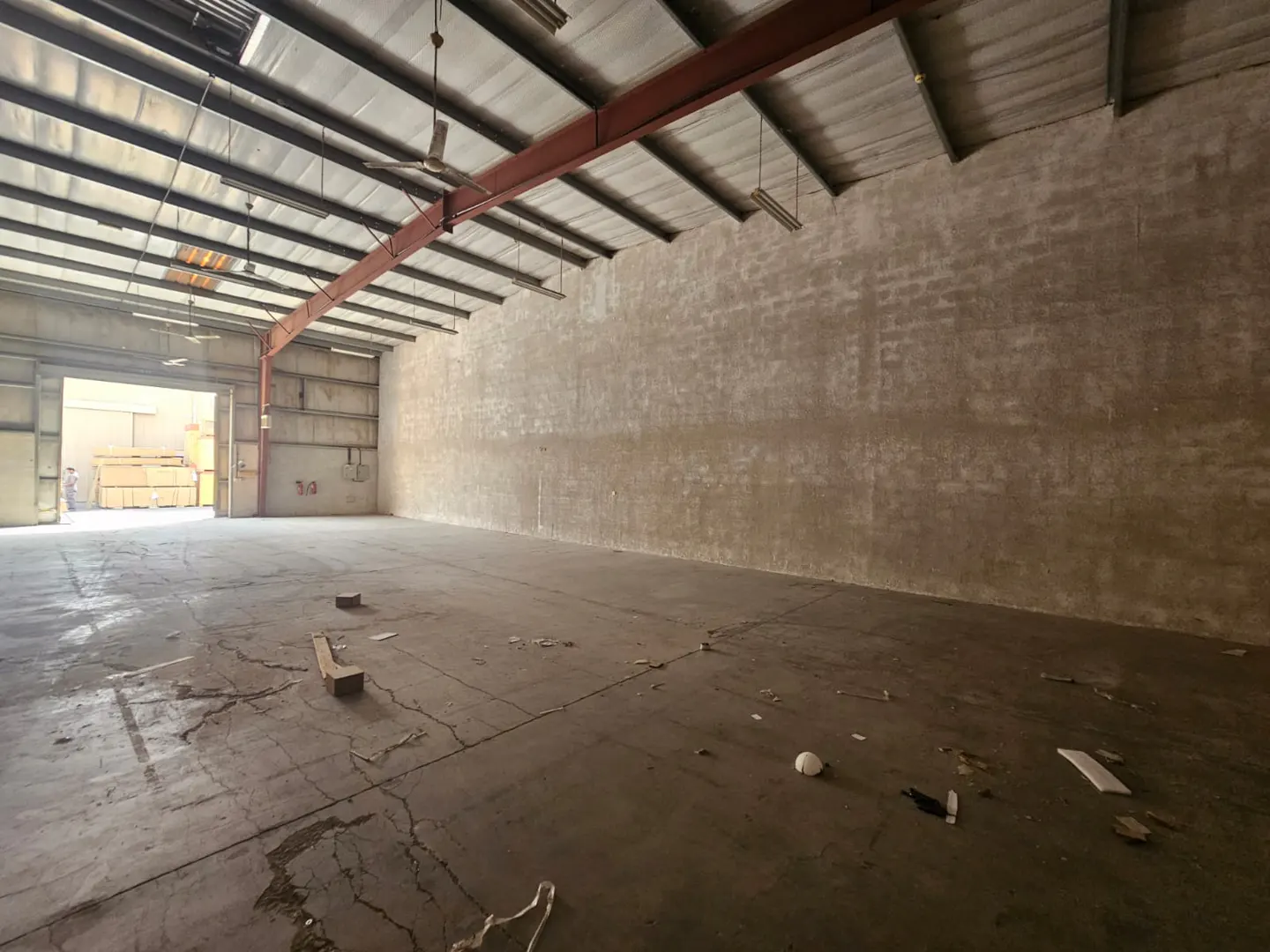 A large, empty warehouse with a concrete floor and walls, and a metal ceiling with red beams.