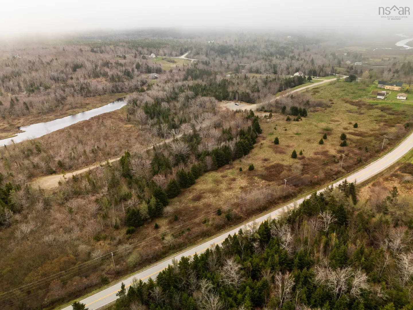 Aerial view of a rural landscape with a road cutting through trees and fields under a cloudy sky.