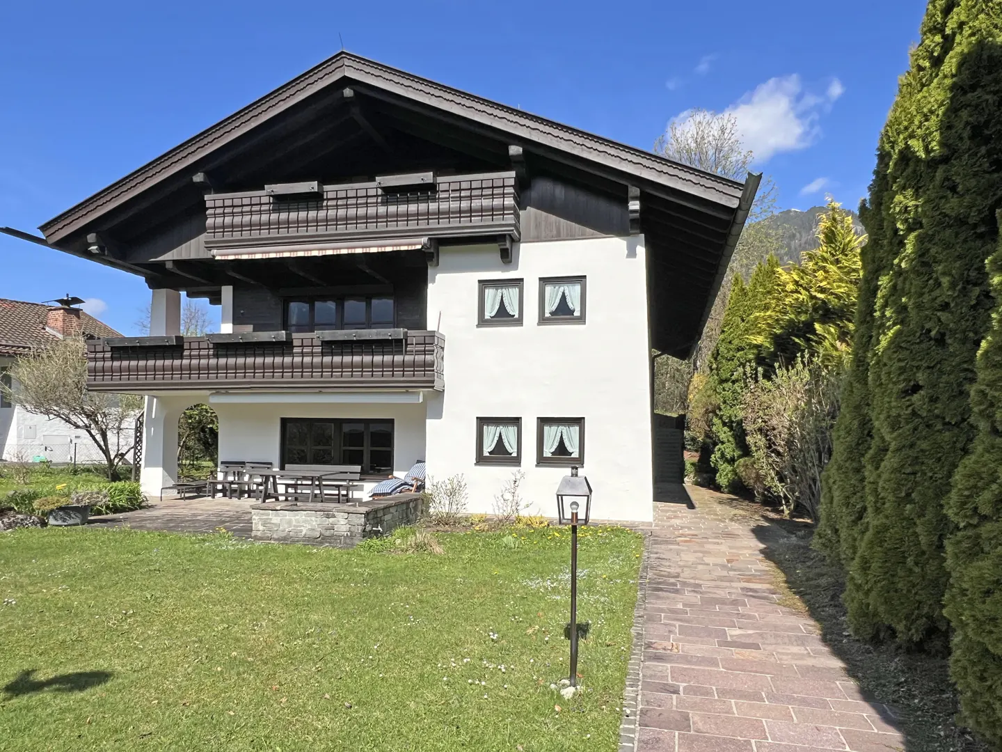 Exterior of a two-story white house with dark brown trim and balconies, green lawn, and stone walkway.