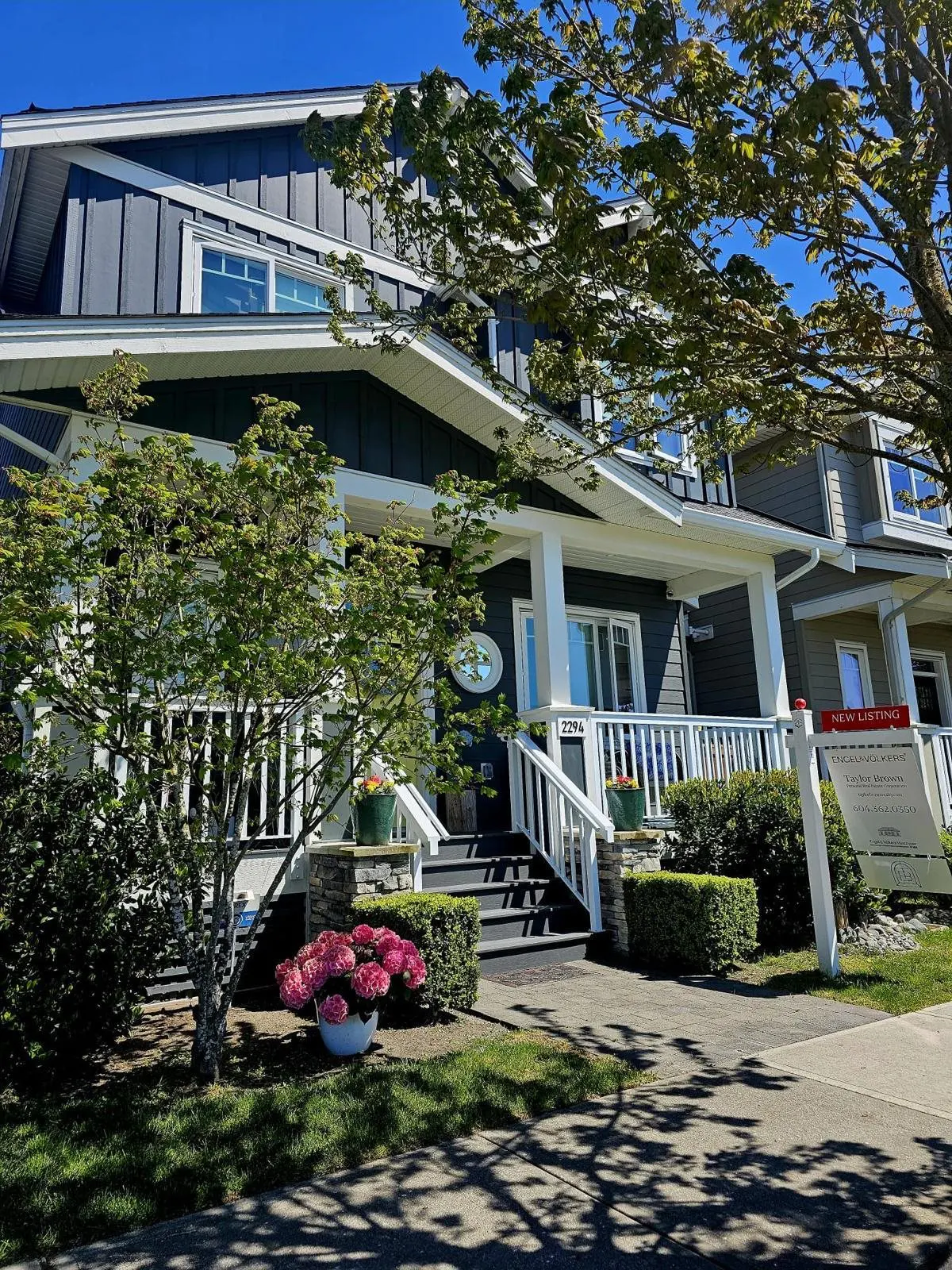 Exterior of a two-story house with dark gray siding, white trim, and a "New Listing" sign on the lawn.