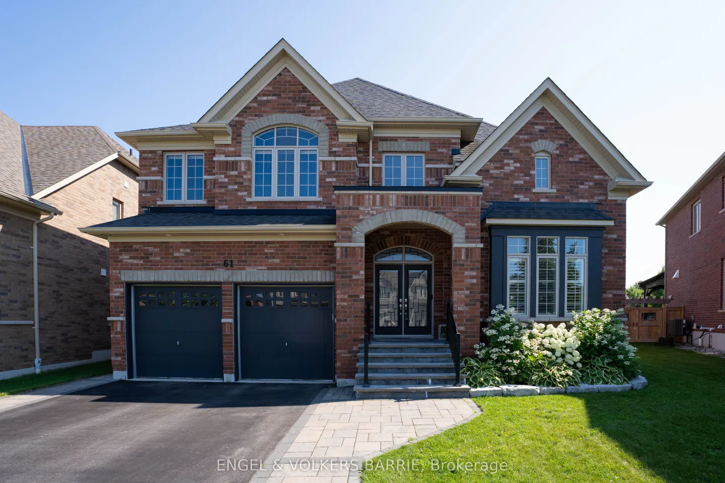 Two-story brick house with a two-car garage, black doors, and a manicured lawn on a sunny day.