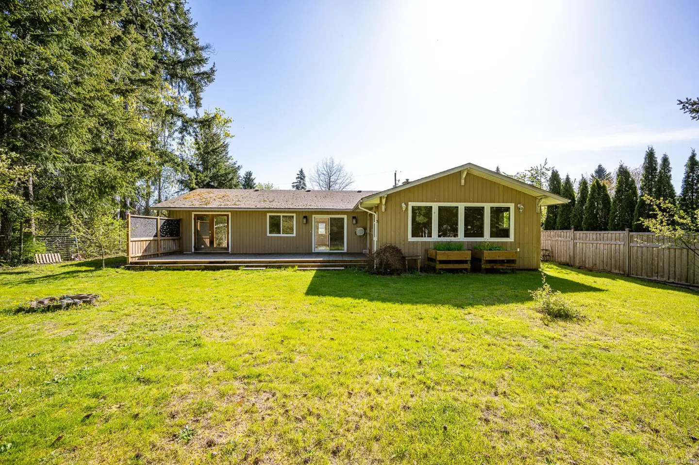 Backyard view of a tan house with a deck, green lawn, and trees under a blue sky.