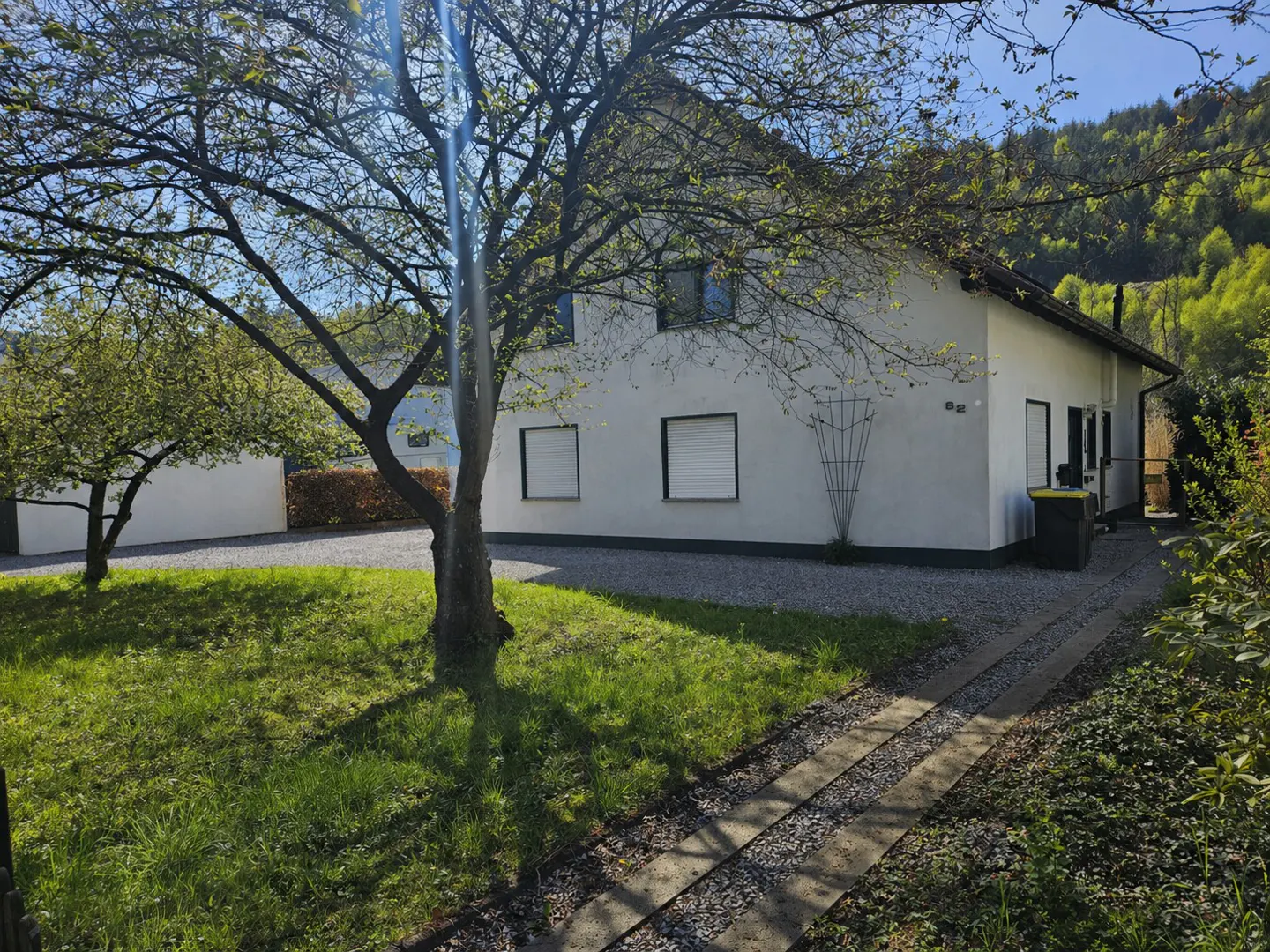 Exterior view of a white, two-story house with green lawn and trees on a sunny day.