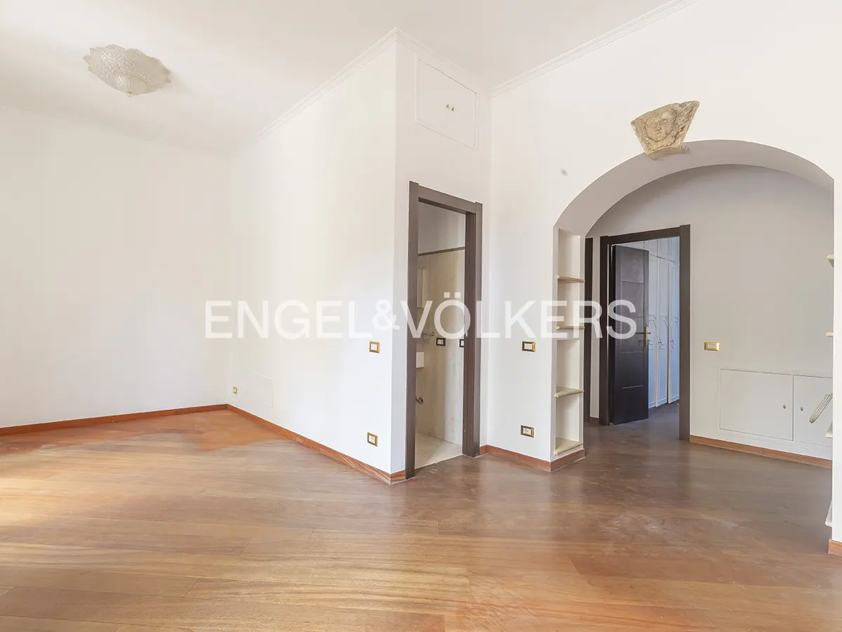 An empty room with hardwood floors, white walls, and an arched doorway. A light fixture is on the ceiling.