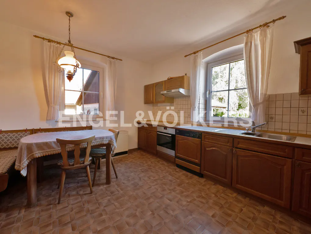 A kitchen with wood cabinets, a table with chairs, and a window with white curtains.