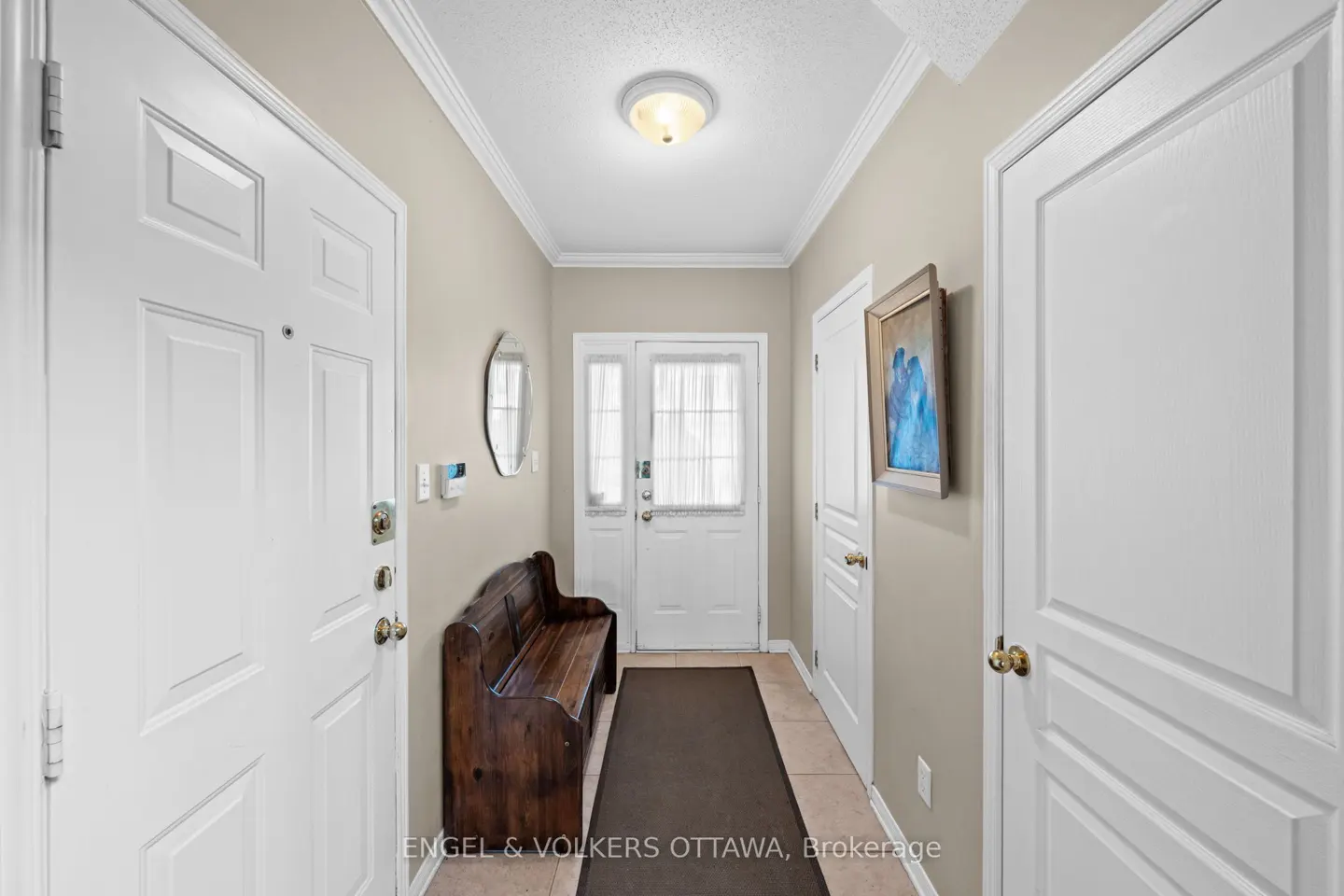 Entryway with white doors, beige walls, and a dark wood bench. A round mirror and framed art hang on the wall. A light fixture is centered on the white ceiling.