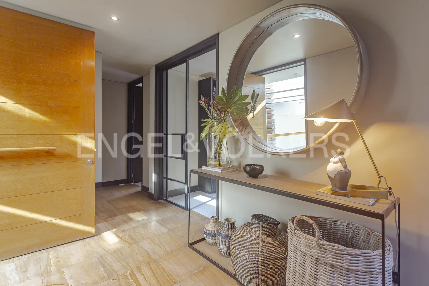 A modern entryway with a wooden door, console table with decor, and a large round mirror.