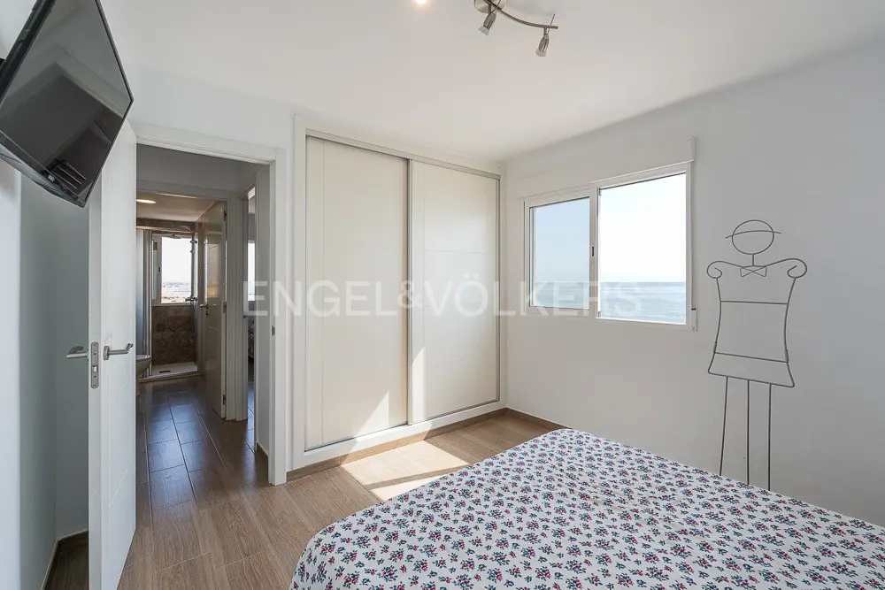 Bedroom with a floral bedspread, white walls, a window with a sea view, and a closet with sliding doors.