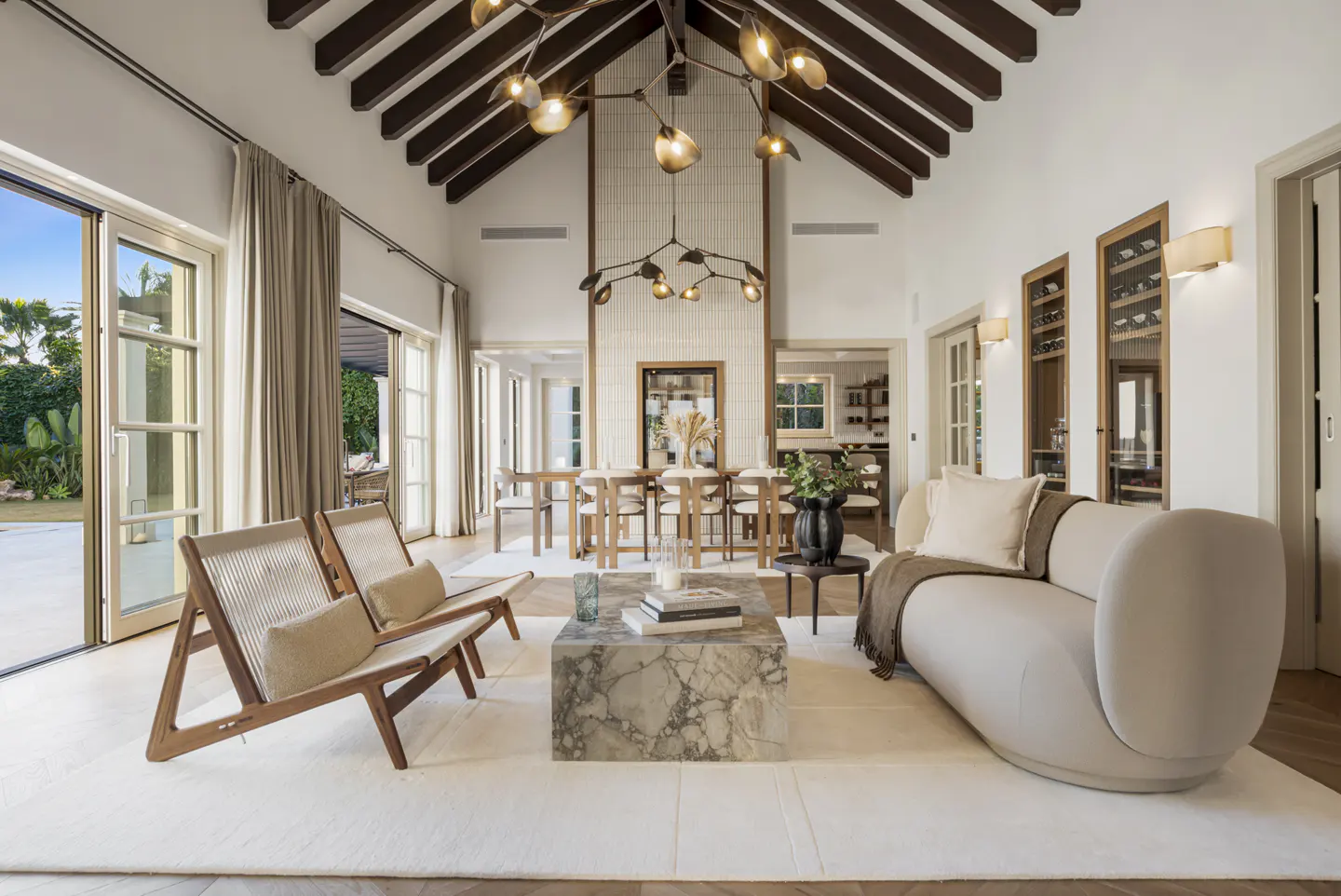 Bright living room with vaulted ceiling, exposed beams, modern chandelier, marble coffee table, and neutral-toned furniture.