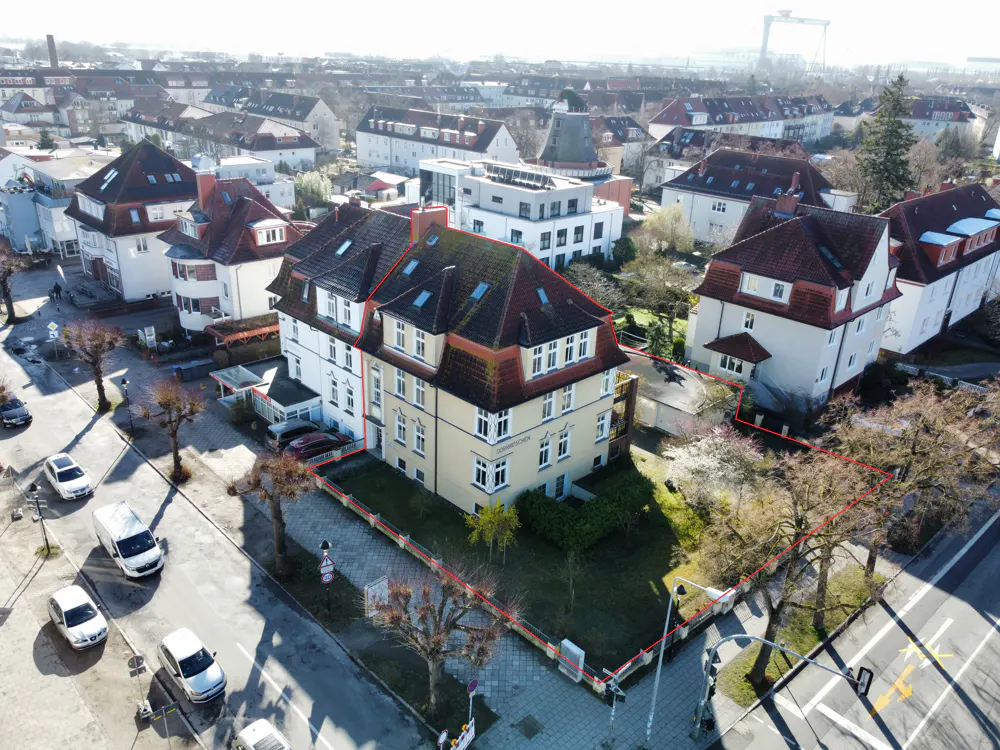 Aerial view of a yellow multi-story apartment building with a red roof, outlined in red, in a residential neighborhood.