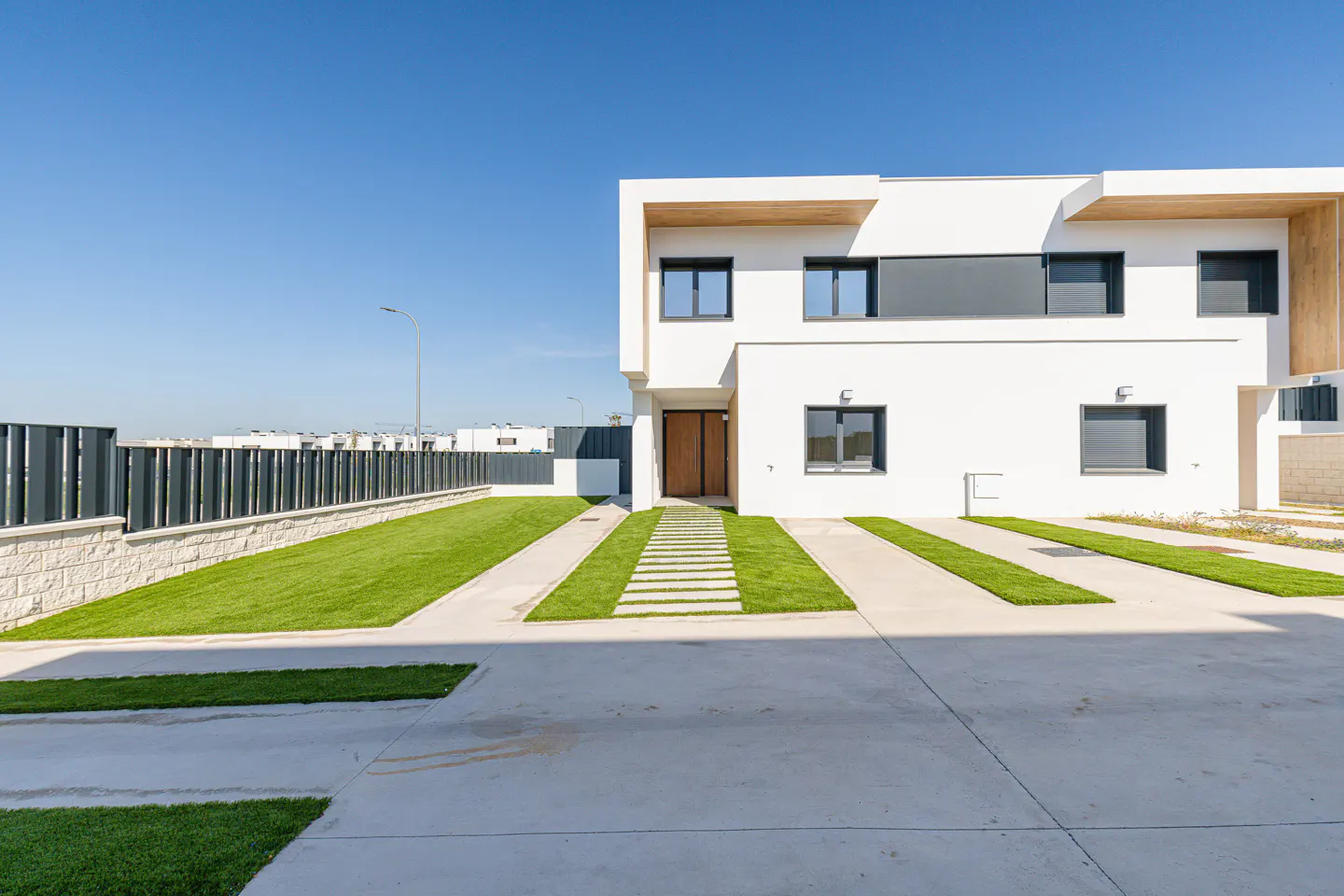 Modern two-story white house with a brown door, black windows, and a green lawn under a clear blue sky.