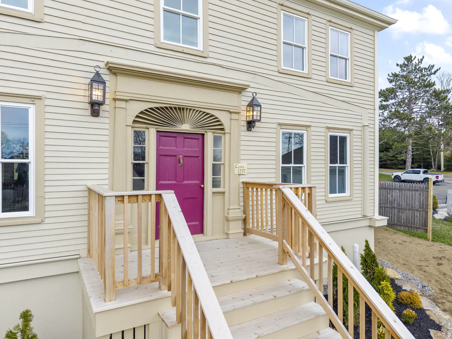 Tan house with a bright pink door and wooden steps leading up to the entrance. Black lanterns flank the door.
