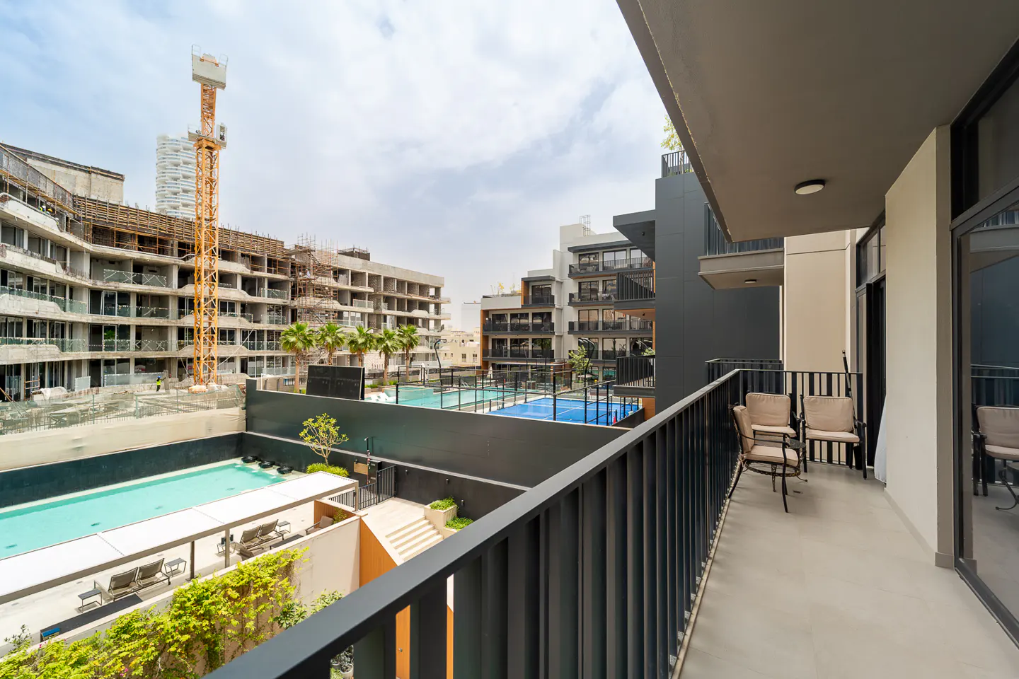 View from a balcony with chairs overlooking a pool, construction site, and buildings on a sunny day.