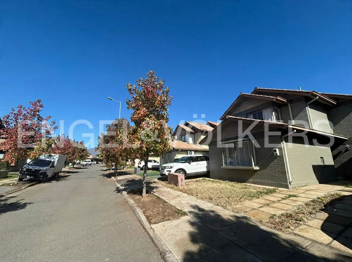 Street view of a two-story house with a white SUV parked in front, trees with red leaves, and a clear blue sky.