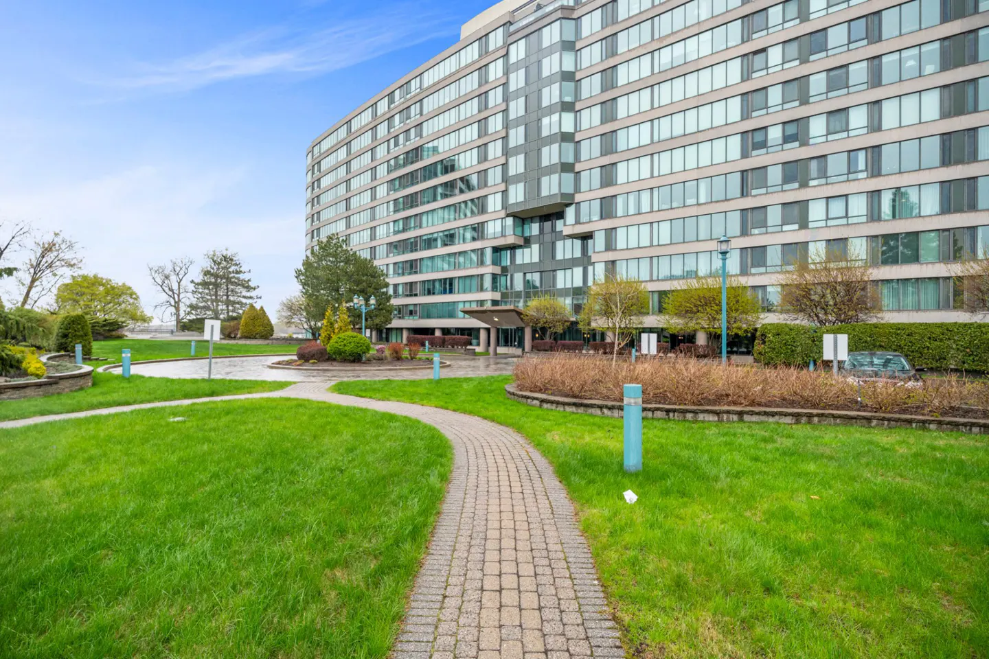 Exterior view of a modern high-rise apartment building with a curved brick walkway and green lawn.