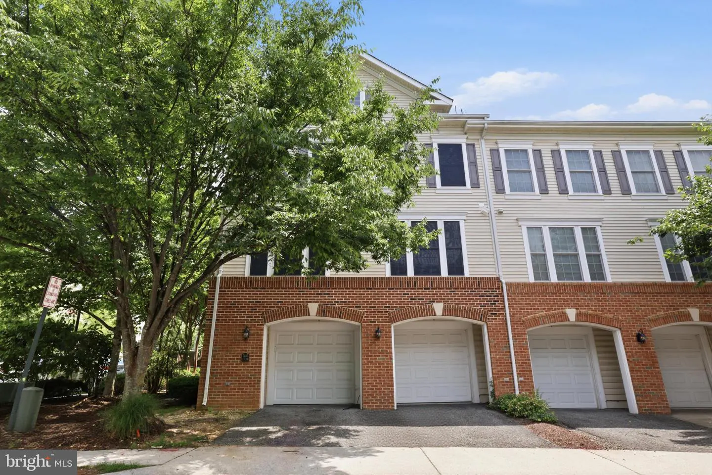 Exterior view of a three-story townhouse with light siding, brick lower level, and multiple white garage doors.