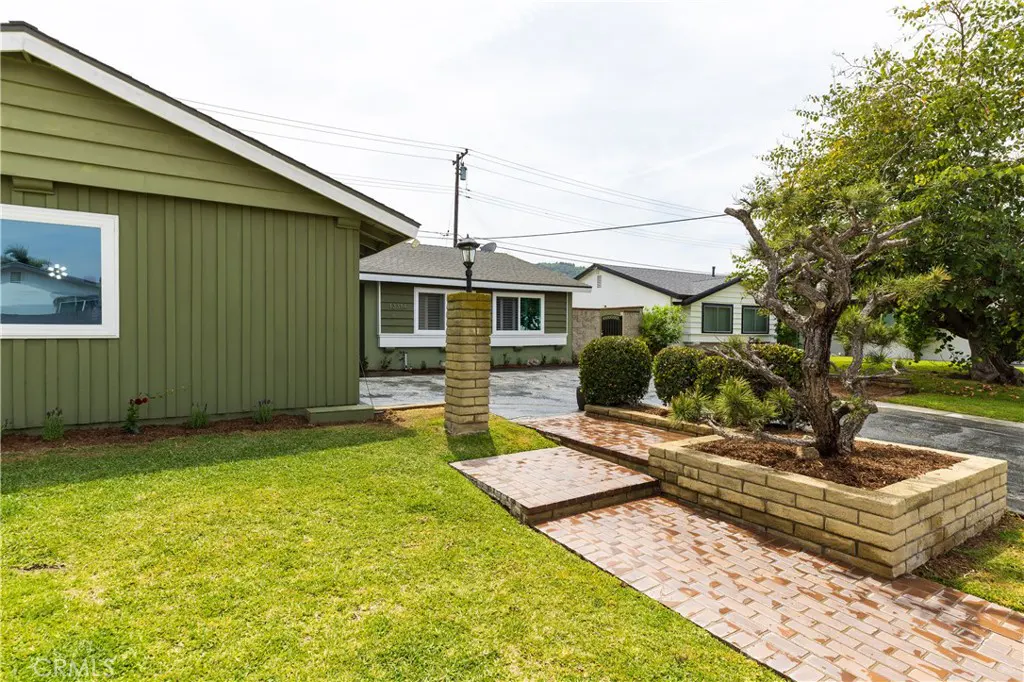 Exterior view of a green house with a brick walkway, a tree in a brick planter, and a green lawn.