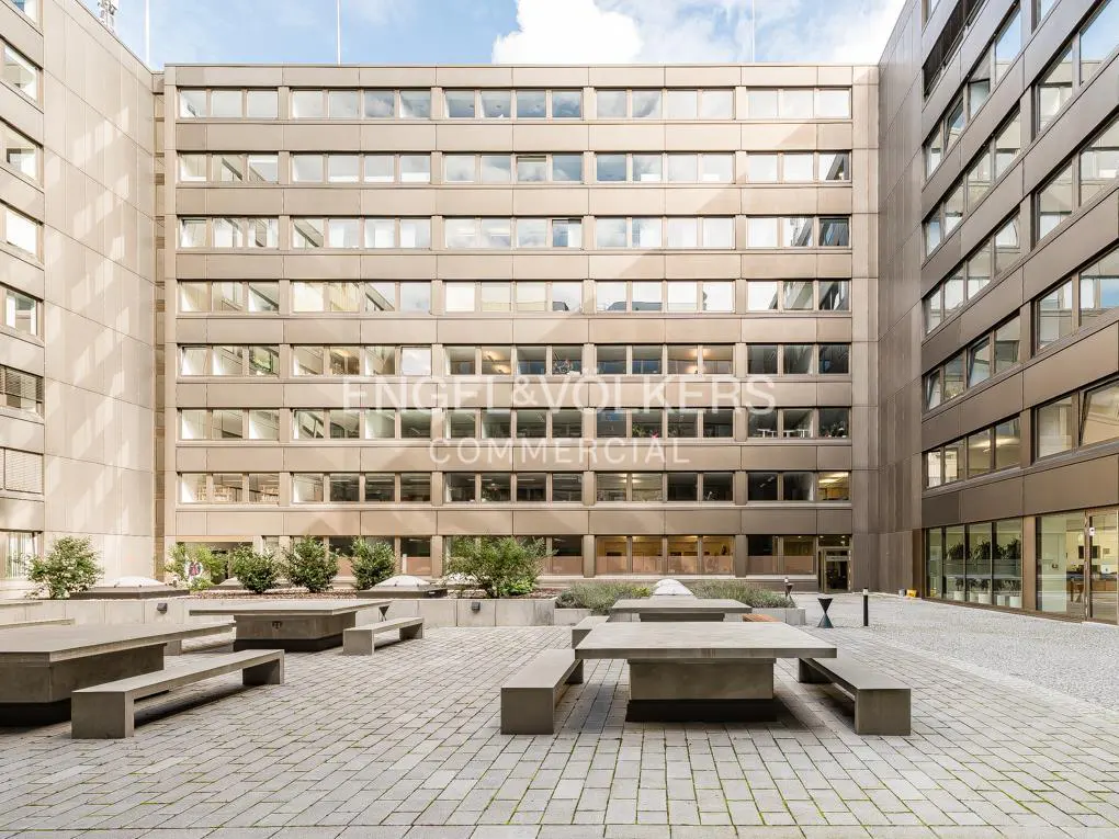Courtyard view of a commercial building with concrete tables, benches, and planters. "Engel & Volkers Commercial" is printed on the building.