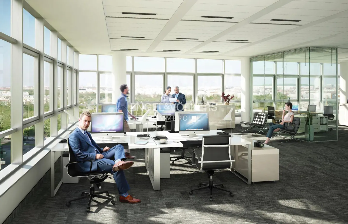Bright, modern office space with white desks, black chairs, and large windows. People are working at computers. A man in a blue suit sits in the foreground.