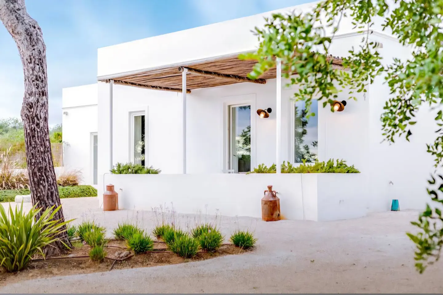 Exterior view of a modern white house with a thatched roof porch, windows, and green plants.